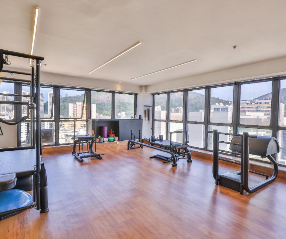 Estúdio amplo da Casa do Corpo em Botafogo, com aparelhos de pilates e grandes janelas com vista para as montanhas do Rio